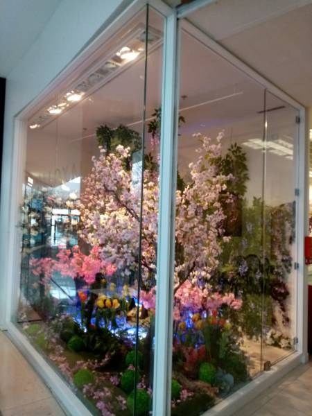 La vitrine d'angle est décorée avec des fleurs et arbres printaniers artificiels.
